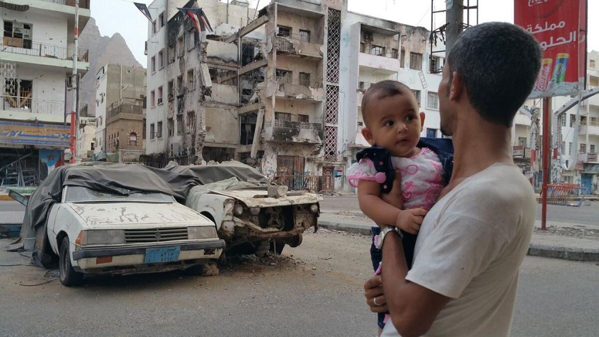 A Yemeni man carrying his daughter looks at a building destroyed during fighting against Houthi fighters in the port city of Aden, Yemen,  July 2015.