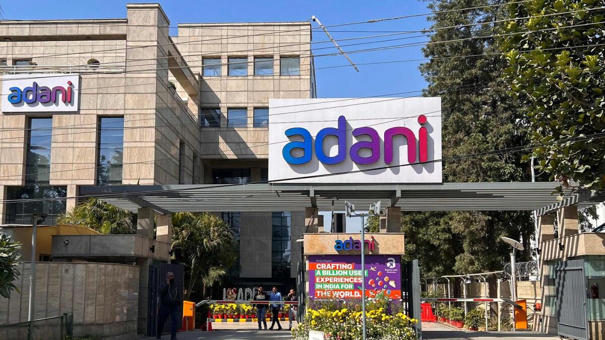 Employees walk past the Adani House corporate building at the institutional area in Gurugram. - AFP