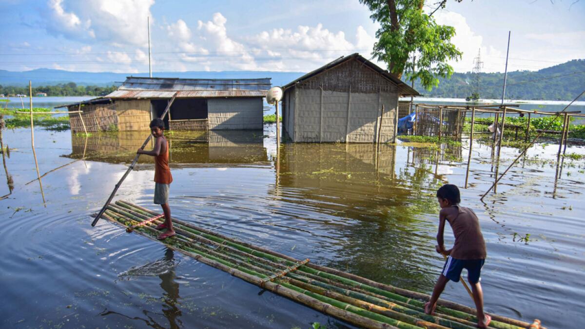 Boys use a makeshift bamboo raft to move across the flooded Baghmari village near Kaziranga in Nagaon district of Assam. Photo: PTI