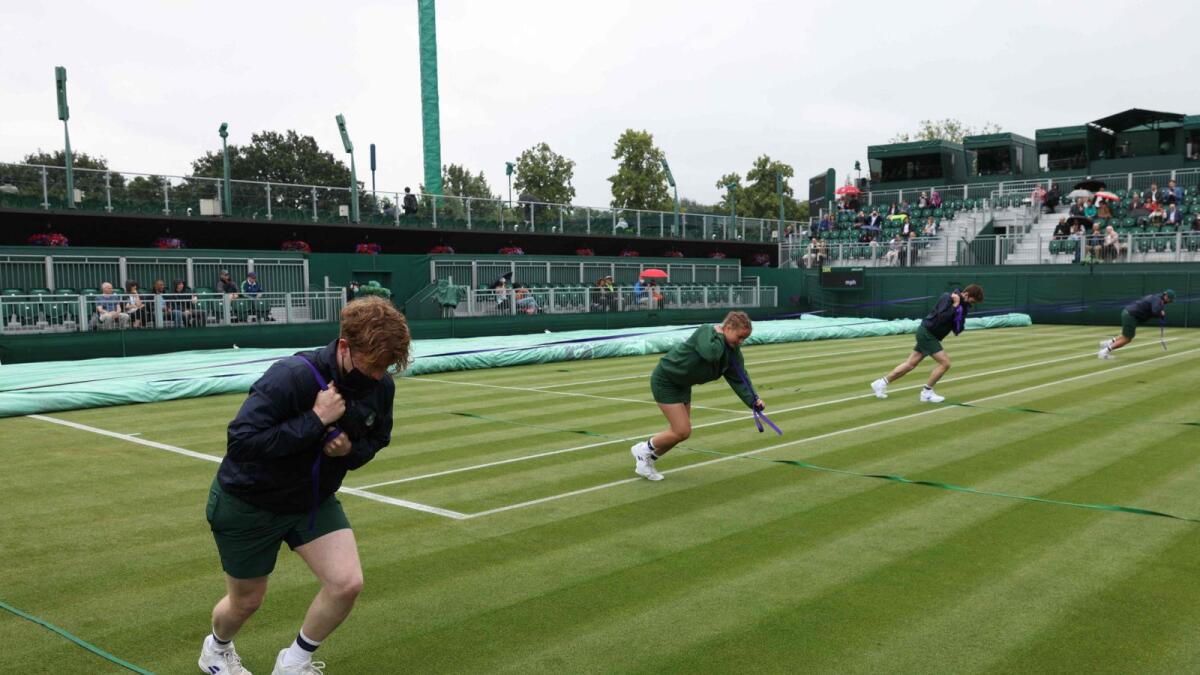 Ground staff pull rain covers in place on an outside court on the first day of the 2021 Wimbledon Championships at the The All England Tennis Club in Wimbledon. — AFP