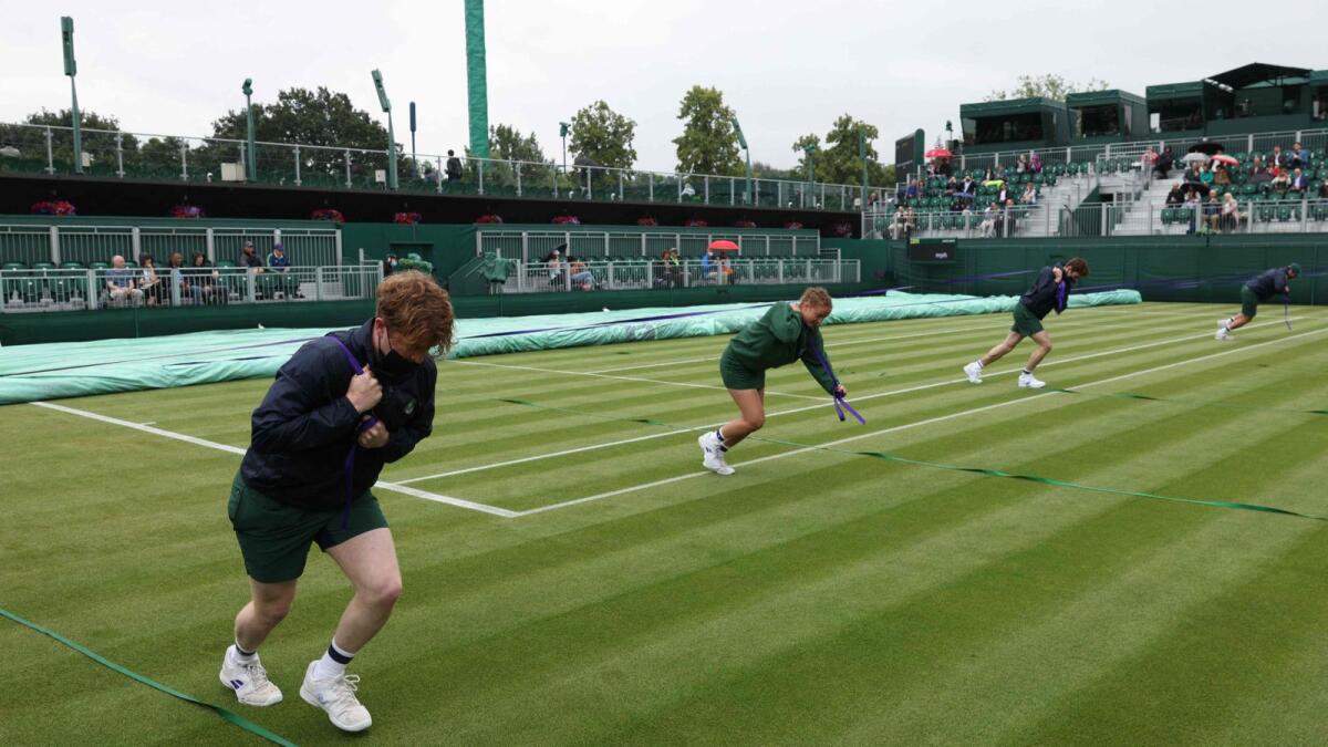Ground staff pull rain covers in place on an outside court on the first day of the 2021 Wimbledon Championships at the The All England Tennis Club in Wimbledon. — AFP