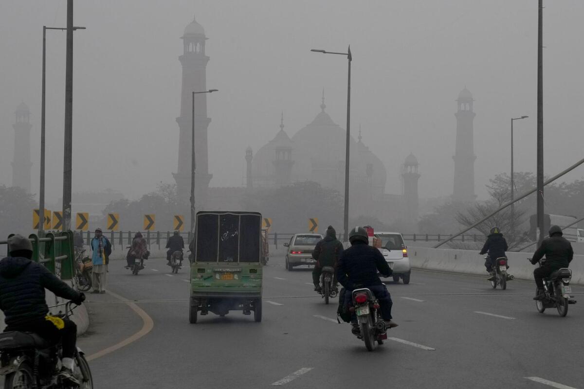 Motorcyclists and vehicles move on a bridge as smog envelops the historical Badshahi Mosque, background, in Lahore on January 5, 2024.— AP