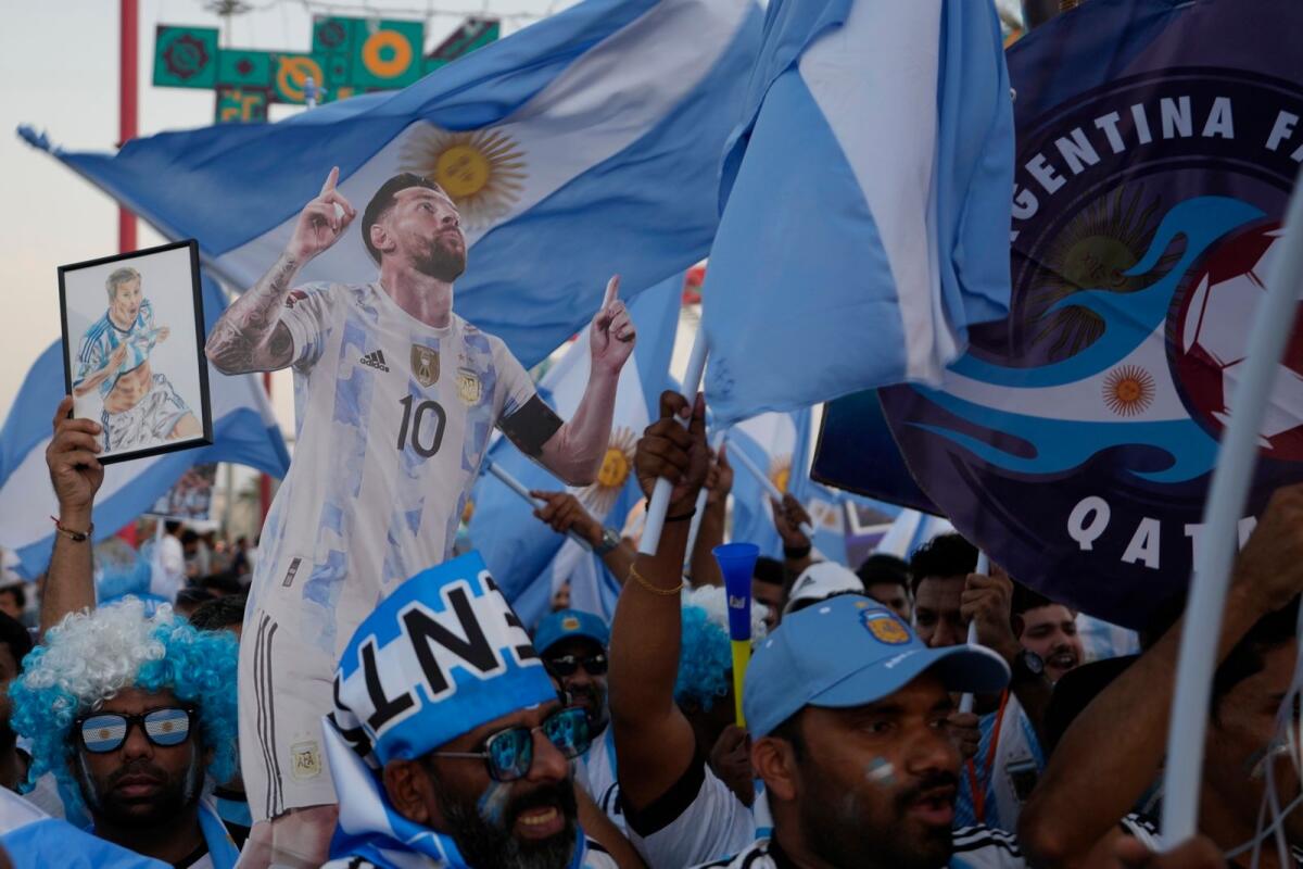 Argentinian fans hold up Lionel Messi pictures as they cheer at the corniche in Doha, Qatar. — AP