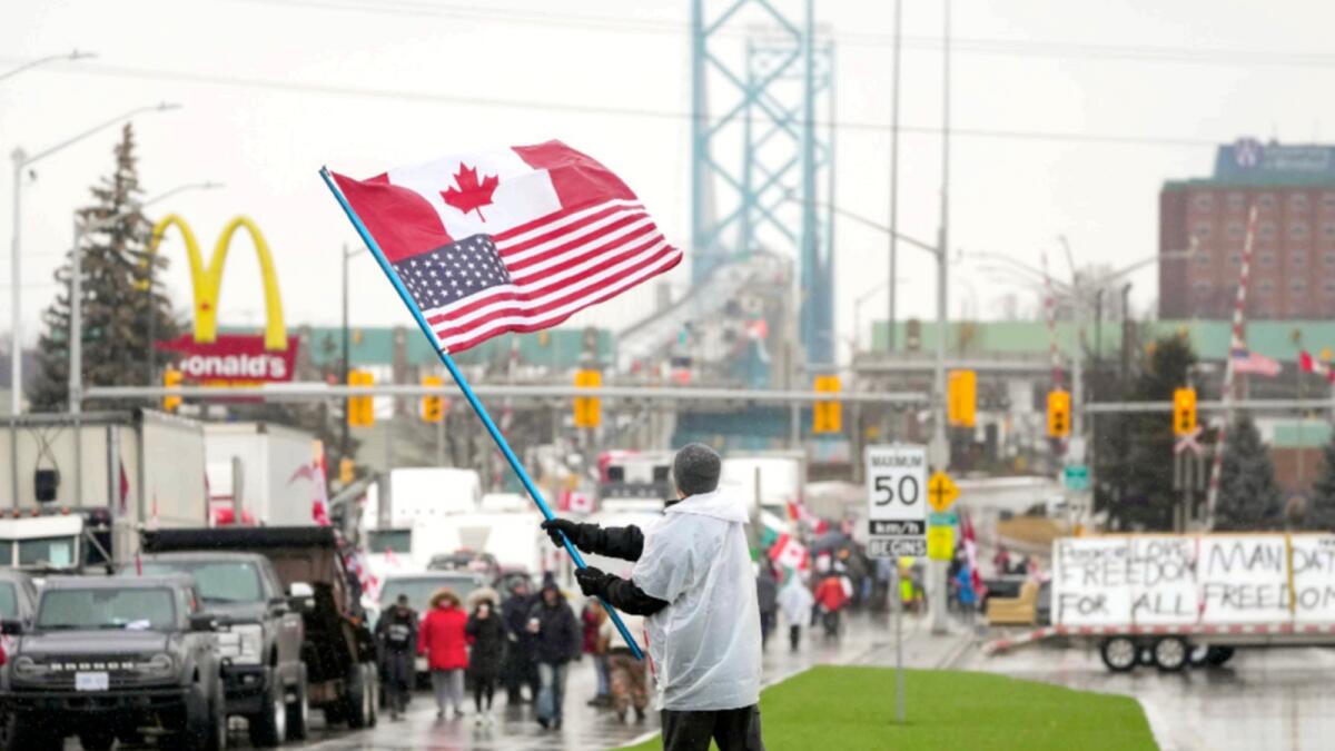 A man waves a Canadian and American flag as truckers and supporters block the access leading from the Ambassador Bridge, linking Detroit and Windsor. — AP