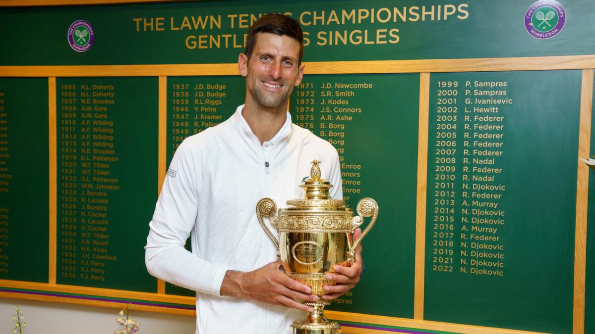 Novak Djokovic holds the trophy with the Wimbledon honours board in the background. (Wimbledon Twitter)