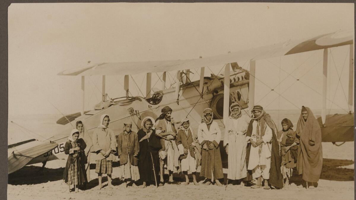 A group portrait of men and children in front of an airplane in Iraq. (1936-1938)