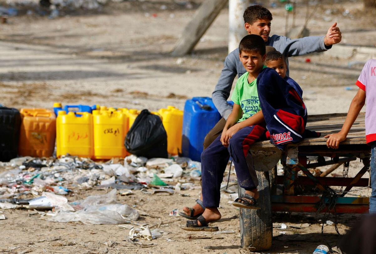 Children sit near containers, as Palestinians collect water, amid a lack of clean and drinking water. Photo: reuters