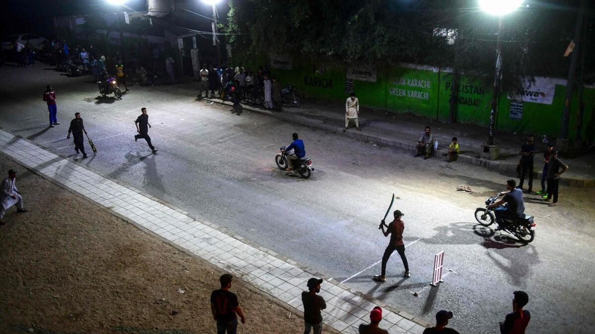 Commuters ride past cricket players during the tape ball night cricket tournament during the holy month of Ramadan in Karachi.— AFP