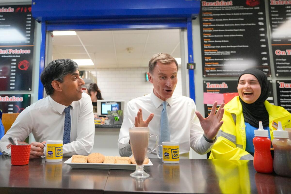 Britain's Prime Minister Rishi Sunak, left, and Britain's Chancellor Jeremy Hunt, centre, have a drink and biscuits as they speak with with employees during a visit to a builders warehouse in London on Wednesday. — AP