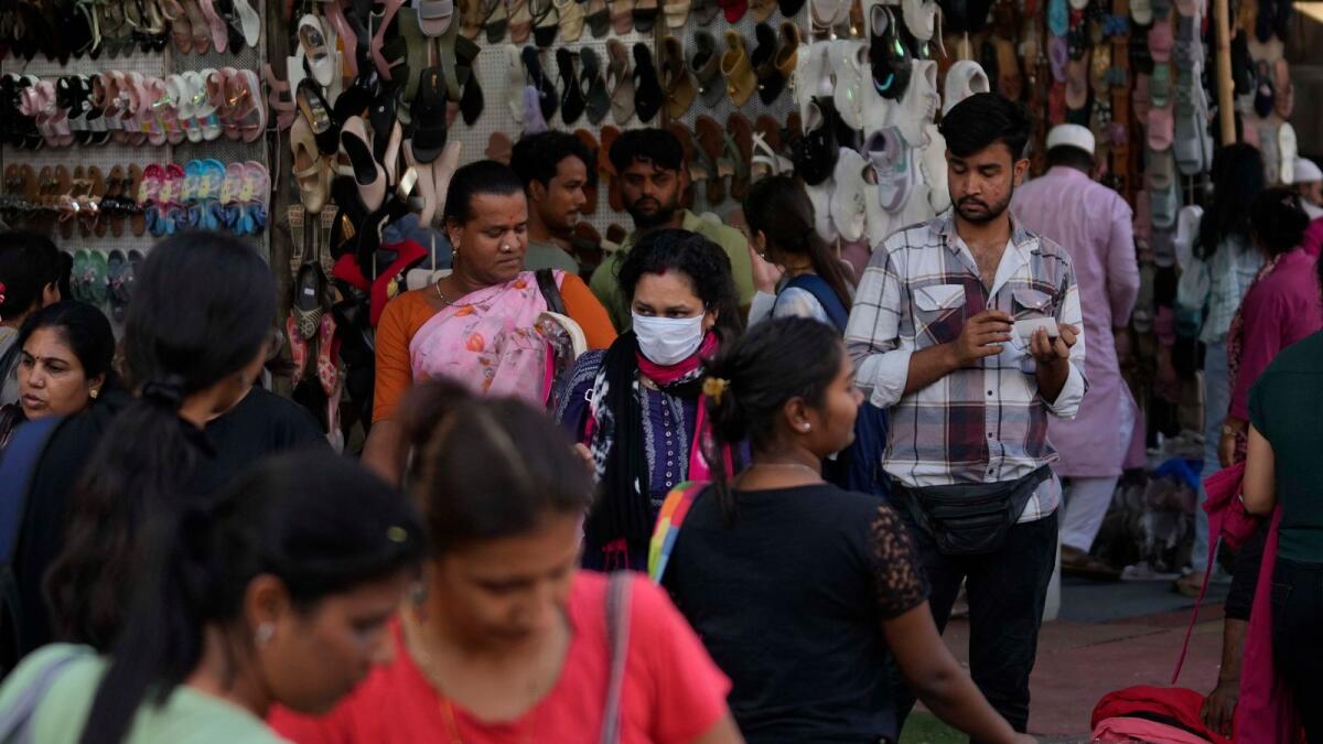 A woman wearing a face mask walks through a busy shopping district in Mumbai. — AP