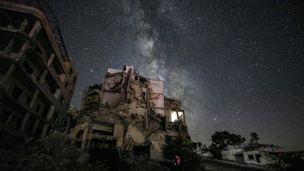 A man using an cell phone while walking past buildings destroyed by prior bombardment in the town of Ariha in Syria's rebel-held northwestern Idlib province, as the Milky Way galaxy is seen in the night sky above.  Photo: AFP