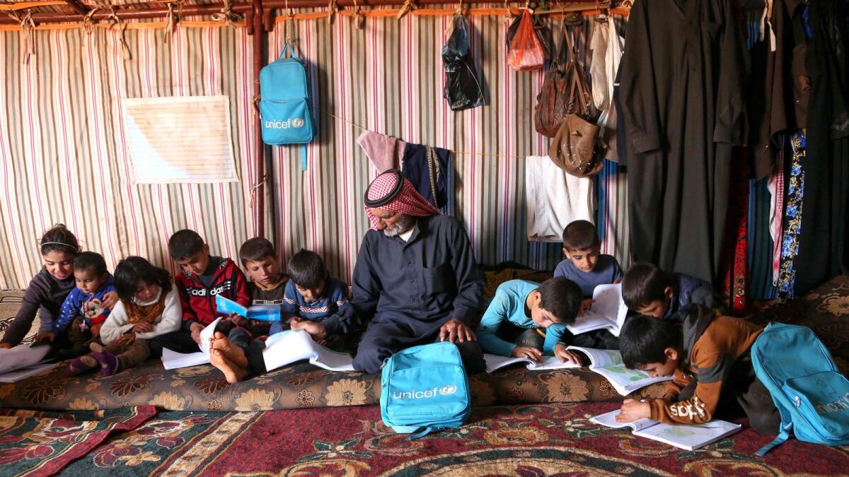 Abderrazaq Khatoun helps his 11 orphaned grandchildren with their school work, inside a tent in an encampment in the village of Harbanoush in the northern countryside of Syria's northwestern province of Idlib.