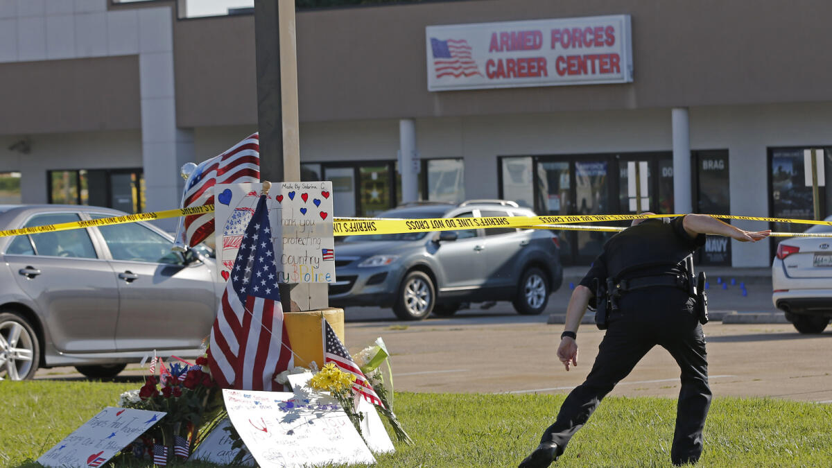 A police officer ducks under tape near a memorial in front of an Armed Forces Career Center on Thursday, July 16, 2015, in Chattanooga, Tenn. A gunman unleashed a barrage of fire at the center and another U.S. military site a few miles apart in Chattanooga, killing several and sending service members scrambling for cover as bullets smashed through the windows. The attacker was also killed. (AP Photo/John Bazemore)