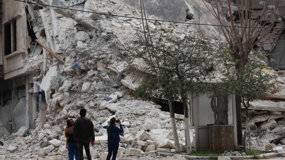 People stand by a building destroyed in recent earthquake in Aleppo, Syria. — AP