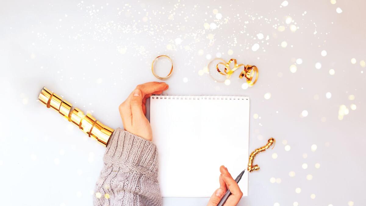 Woman hands holding clear white notebook, golden sparkles, new year, flat lay.