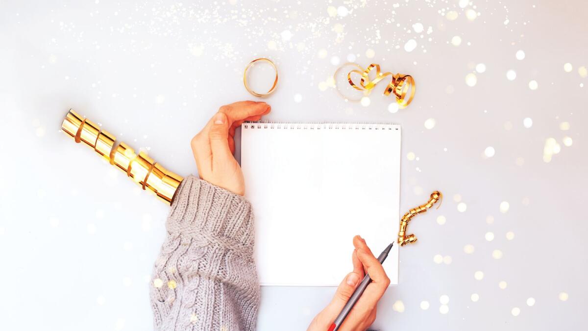 Woman hands holding clear white notebook, golden sparkles, new year, flat lay.