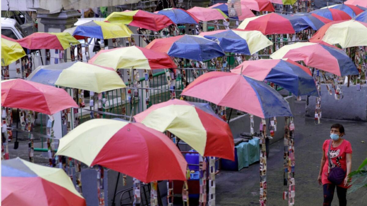A woman wearing a face mask to help curb the spread of the coronavirus walks under decorative umbrellas in Taguig, Philippines. — AP