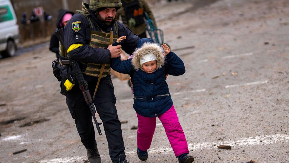 A Ukrainian police officer runs while holding a child as the artillery echoes nearby, while fleeing Irpin on the outskirts of Kyiv, Ukraine. (AP)