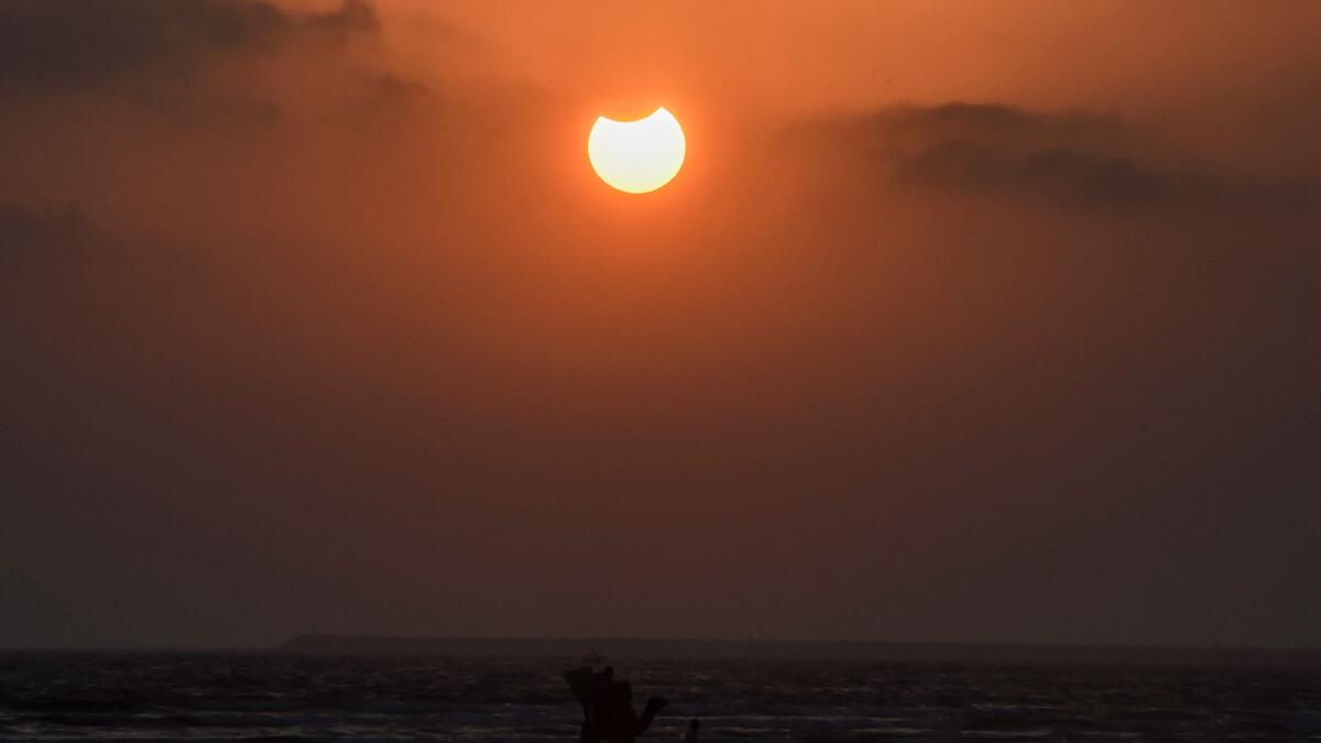 A man leads a camel along a beach as the moon partially obscures the sun in Karachi, Pakistan. (AFP)