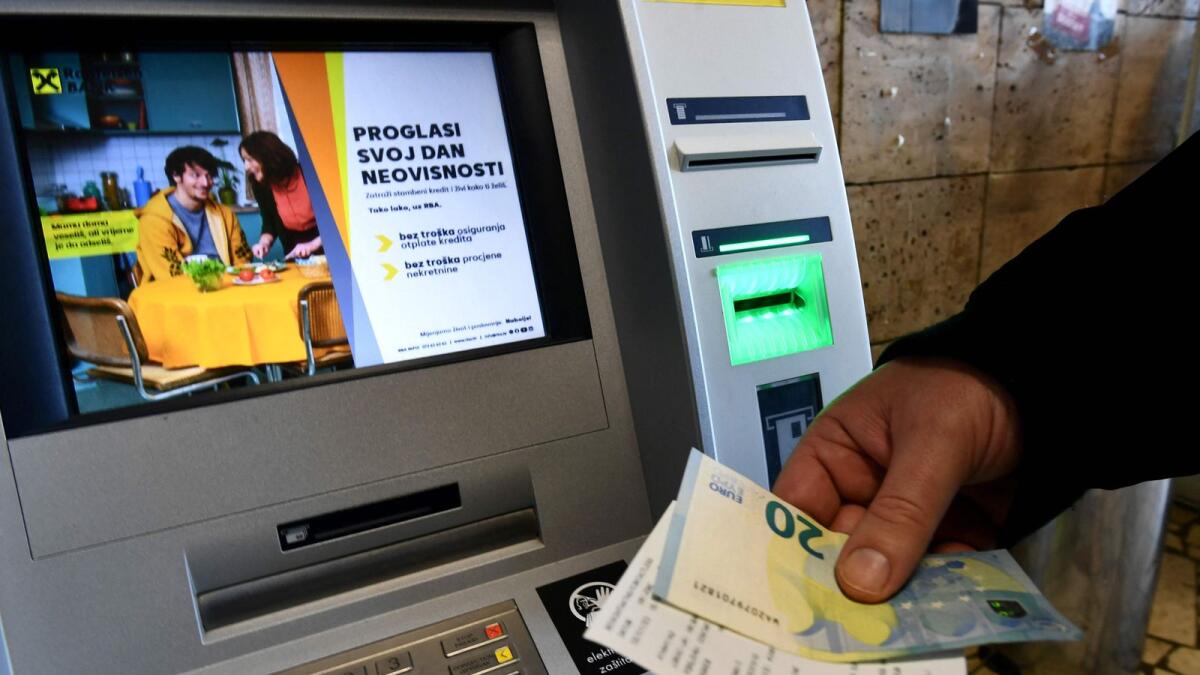 A man withdraws euro banknotes from an ATM, in Zagreb. — AFP