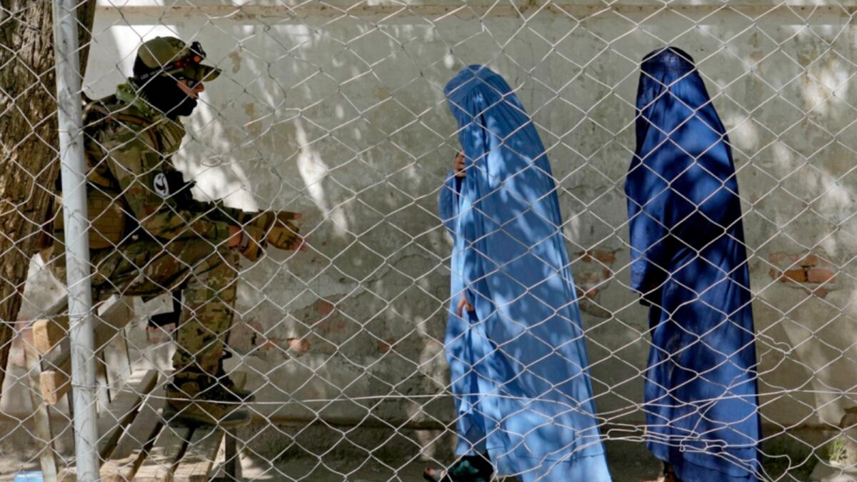 A Taliban fighter stands guard as two women enter the government passport office in Kabul. — AP