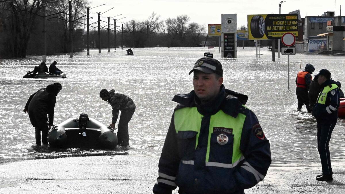 Traffic police officers stand on a flooded street as rescuers on inflatable boats evacuate residents of the city of Orsk, Russia's Orenburg region, on Monday.— AFP