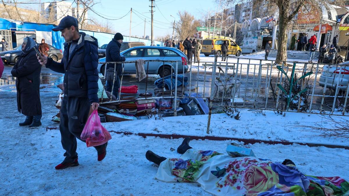 People walk past bodies of victims killed during the shelling that Russian officials in Donetsk said was conducted by Ukrainian forces. — AP