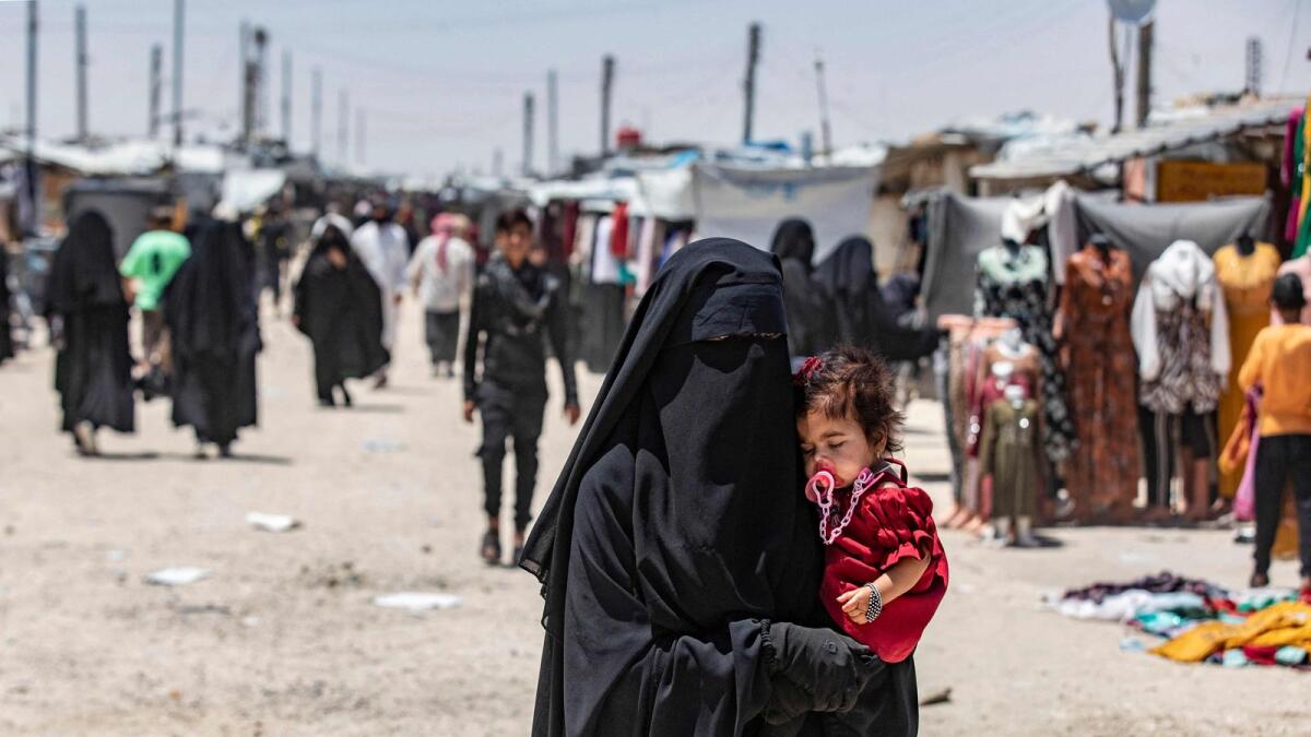 A woman carries a child as she walks through the al-Hol camp in Syria's northeastern AlHasakah Governorate, on October 10, 2023. — AFP