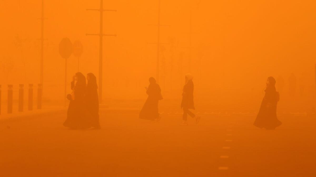 Pedestrians cross a road amidst a severe dust storm in Kuwait City on May 23, 2022. Photo: AFP