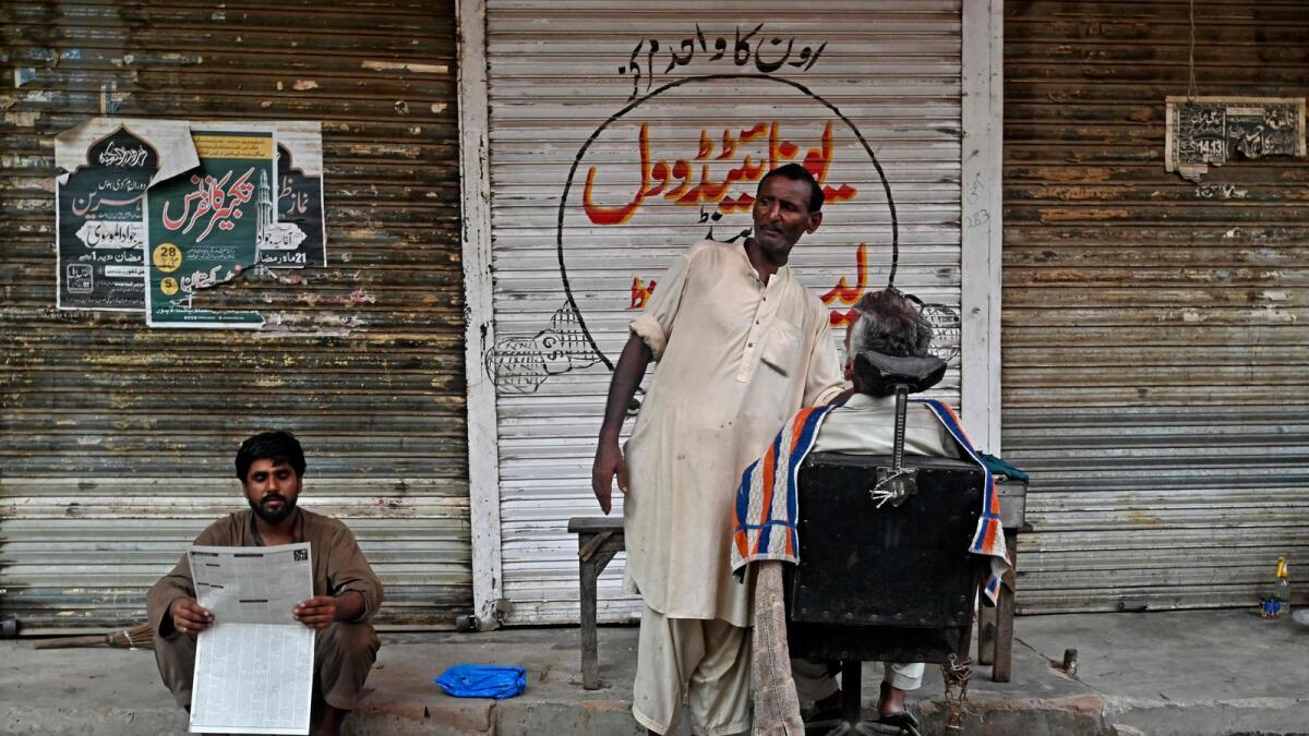A barber attends his customer along a street in Lahore on July 21, 2023. — AFP file photo used for illustrative purpose only