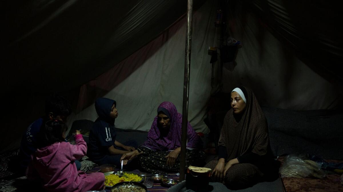 Randa Baker, Right, and her family, who were displaced by the Israeli bombardment of the Gaza Strip, end their fast on the first day of the  holy month of Ramadan at a makeshift tent camp in the Muwasi area, southern Gaza, on March 11, 2024. — AP