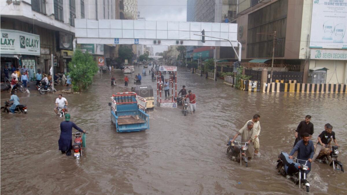 Motorcyclists and people wade through a flooded road in a business district after a heavy rainfall in Karachi. — AP photos
