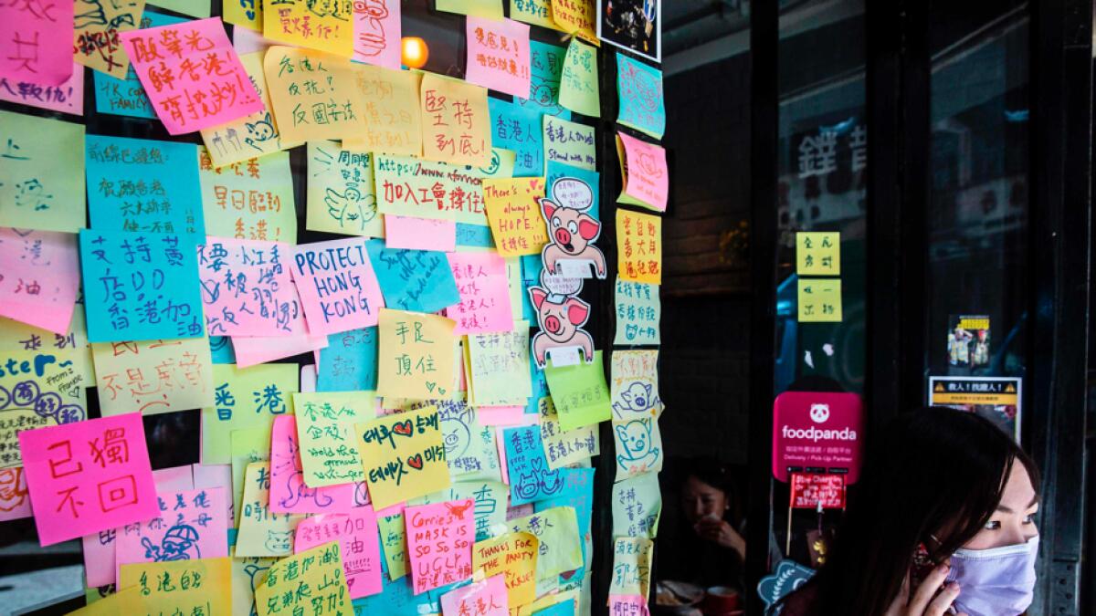 A woman stands next to layers of notes on a Lennon Wall with messages of support for the pro-democracy protests outside a restaurant in Hong Kong. Photo: AFP