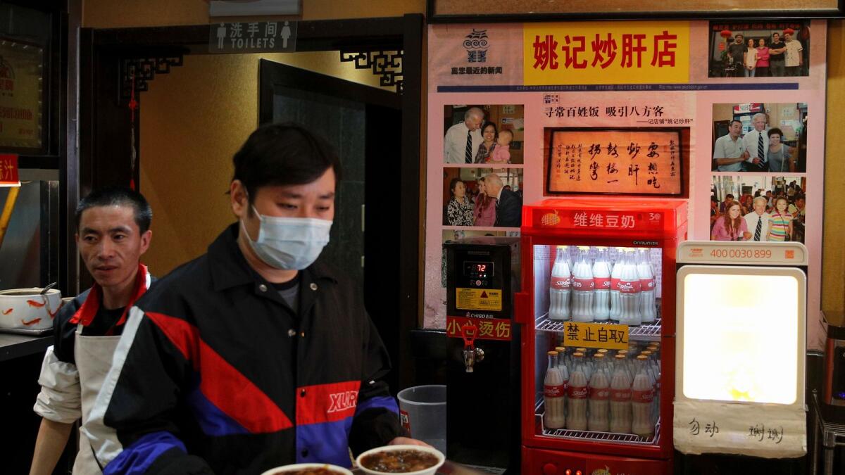 A man wearing a face mask carries his foods past photos of Joe Biden on display at a restaurant which he visited several years ago, in Beijing, on Sunday.