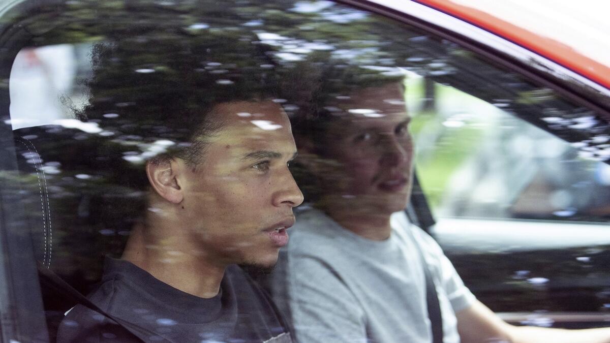 Newcomer Leroy Sane, left, sits in a car as he leaves the FC Bayern training ground in Munich