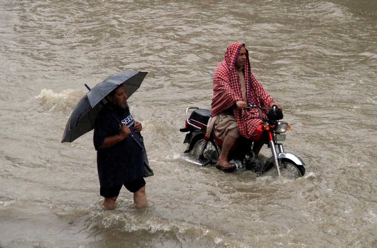A man holds an umbrella as he walks through floodwaters during heavy rain in Lahore, Pakistan.- Reuters