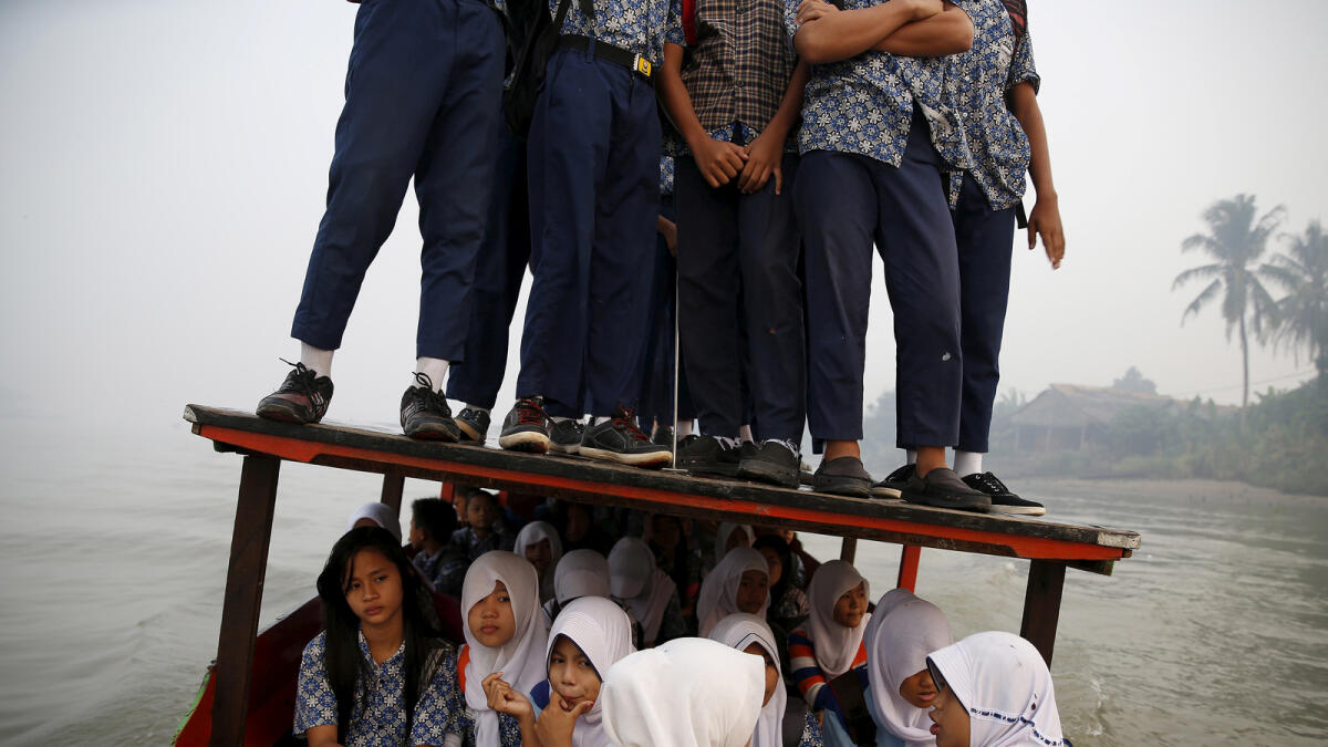 Students stand on the roof of a wooden boat as haze blankets the Musi River while they travel to school in Palembang, on Indonesia's Sumatra island, September 10, 2015.  Reuters