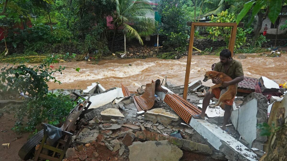 A resident carries a dog amid debris of his damaged house after flash floods caused by heavy rains in Kerala. – AFP