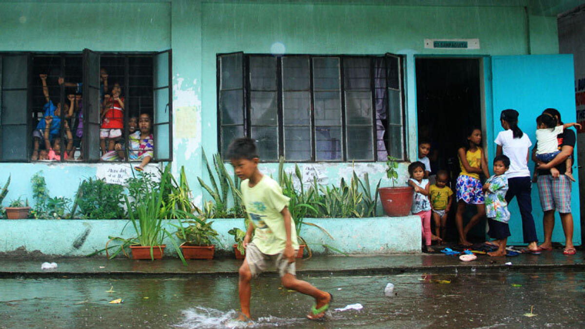 A young evacuee wades through flooded school grounds while others look on from a school building being used as an evacuation center in the city of Legaspi in Albay province, south of Manila on December 14, 2015, as typhoon Melor approaches the city. (AFP photo)