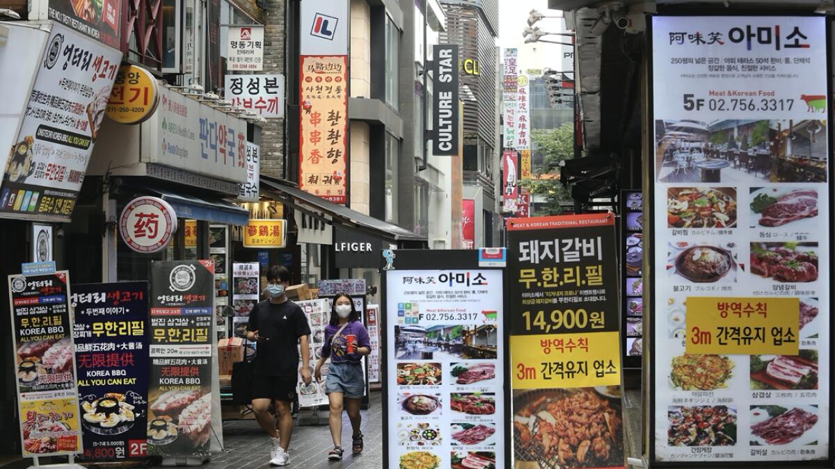 People wearing face masks to help protect against the spread of the coronavirus pass by banners showing the menu items of restaurants in Seoul, South Korea. South Korean officials are considering reducing working hours of restaurants and cafes as the country counted its 15th straight day of triple-digit jumps in coronavirus infections. Photo: AP