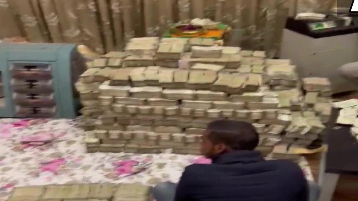 An Indian tax official sits in front of cash recovered from industrialist Piyush Jain's residence. — ANI