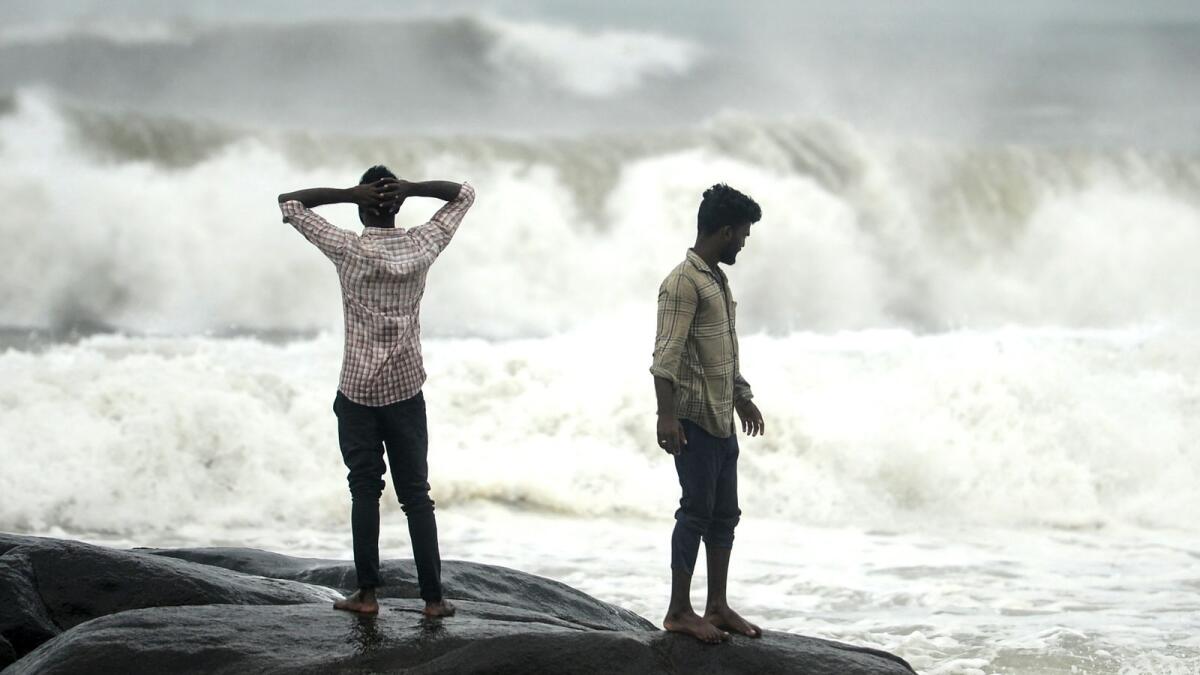People stand on a rock while waves lashes over at Kovalam beach as cyclone Nivar approaches the eastern Indian coast, in Chennai on November 24, 2020. (Photo by Arun SANKAR / AFP)