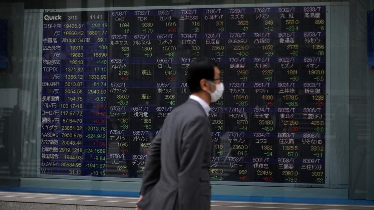 A man wearing protective face mask, following an outbreak of the coronavirus disease, walks in front of a stock quotation board outside a brokerage in Tokyo. - Reuters