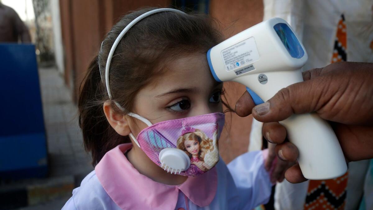 A worker checks body temperature of a student upon her arrival at a primary school in Lahore.