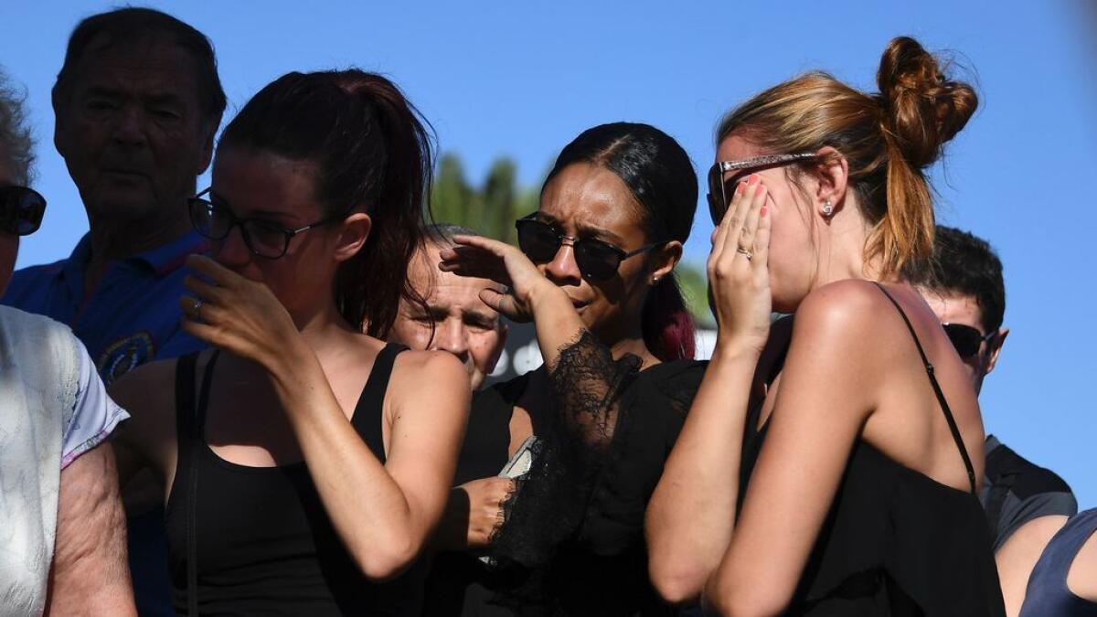 People react as they stand next to the make-shift memorial where people laid flowers to pay tribute to the victims the day after a gunman smashed a truck into a crowd of revellers celebrating Bastille Day