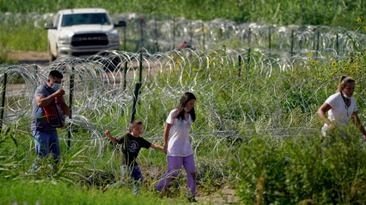 Migrants walk along concertina wire toward Border Patrol officers after illegally crossing the Rio Grande from Mexico into the US at Eagle Pass, Texas. — AP file