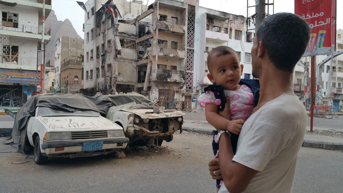 A Yemeni man carrying his daughter looks at a building destroyed during fighting against Houthi fighters in the port city of Aden.
