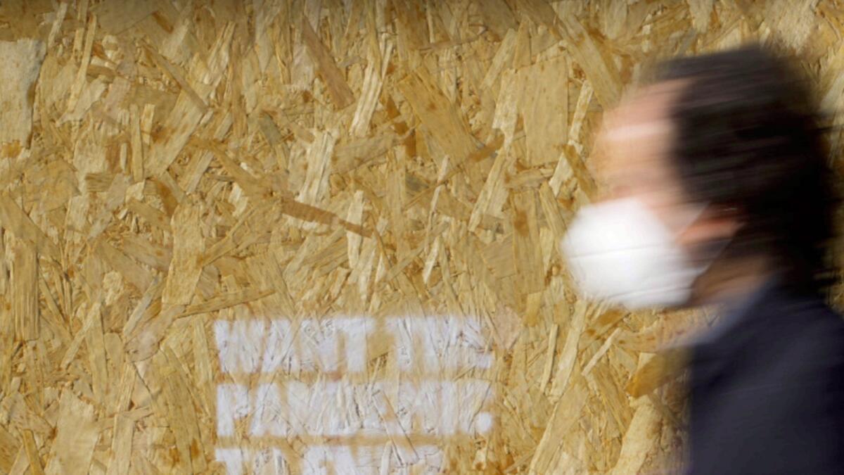 A man wearing a face mask walks past a wooden board with graffiti reading 'Want the pandemic to end?' in Rome. — AP