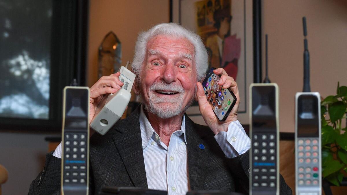 Engineer Martin Cooper holds in his right hand a contemporary copy of the original cell phone and his latest iPhone in Del Mar, California. - AFP