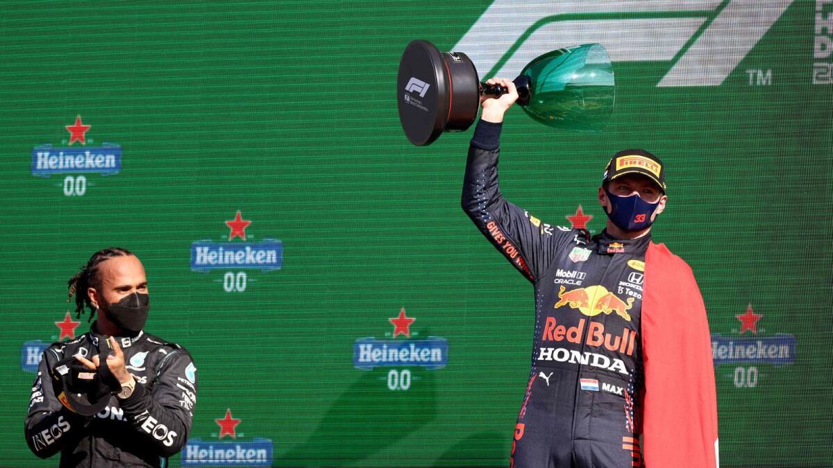 Red Bull's Dutch driver Max Verstappen (right) holds the winner's trophy as Mercedes' British driver Lewis Hamilton applauds on the podium of the Zandvoort circuit after the Netherlands' Formula One Grand Prix. — AFP